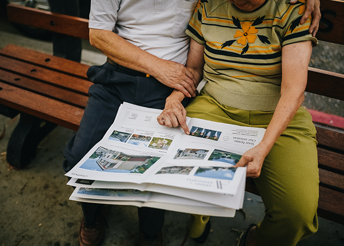 couple sitting on bench reading real estate section of local newspaper