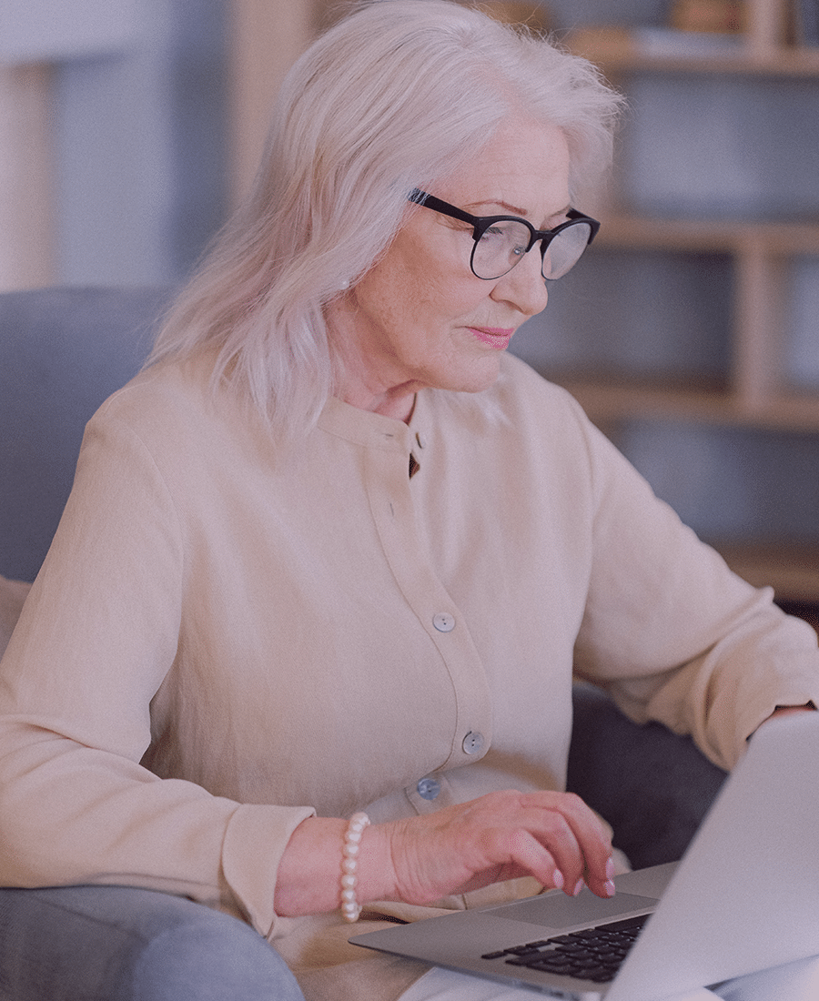 older professional real estate agent woman in cardigan with glasses on laptop computer