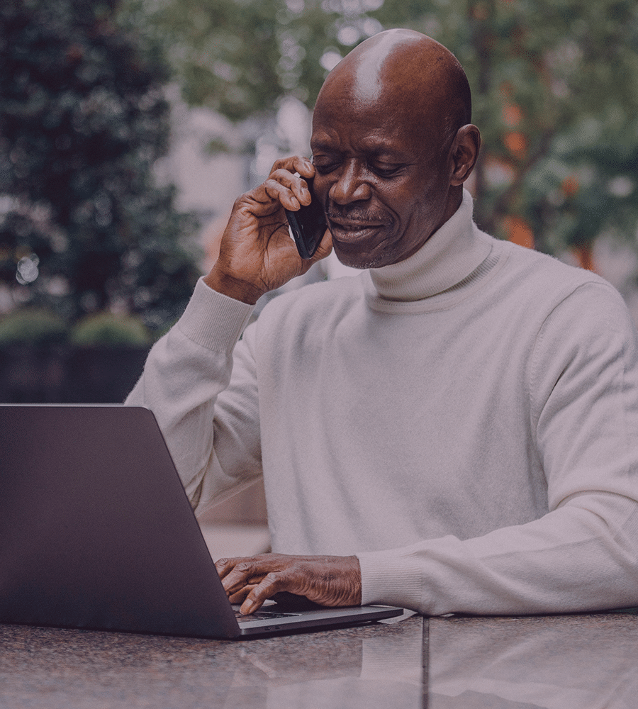 older real estate agent black male talking on phone while on laptop outside