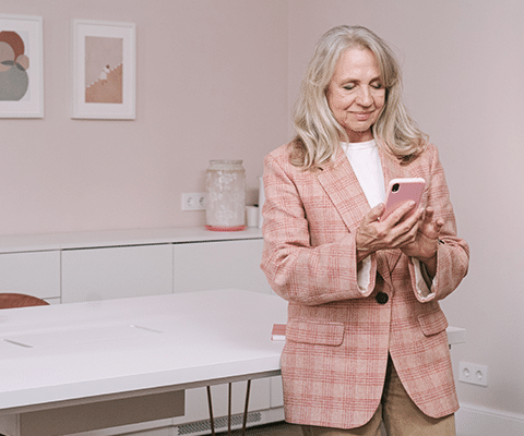 professional older white woman wearing pink holding a pink phone checking her gmail account