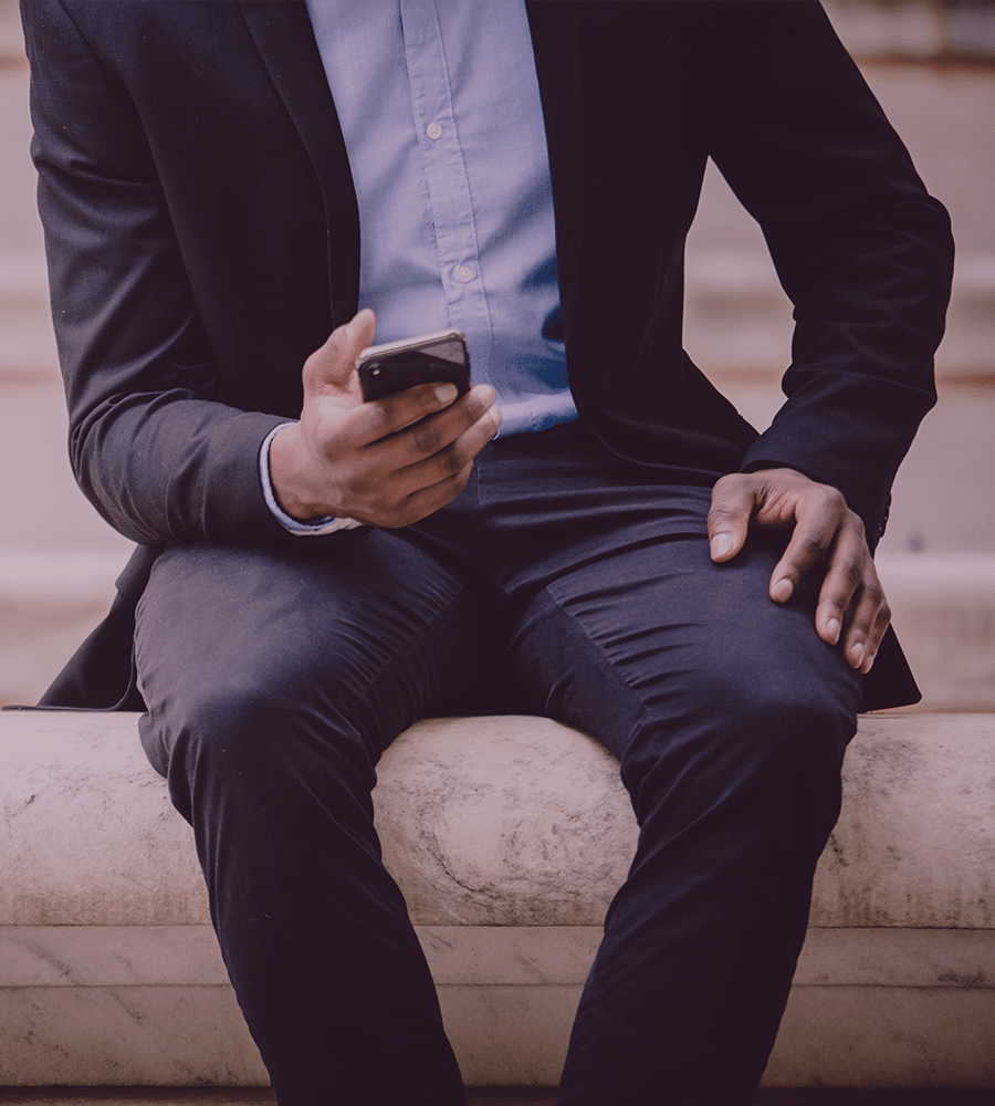 professionally dressed man looking at phone on concrete bench