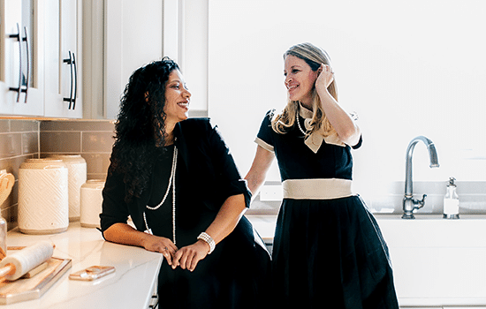 two female real estate agents wearing black dresses standing and smiling in residential kitchen