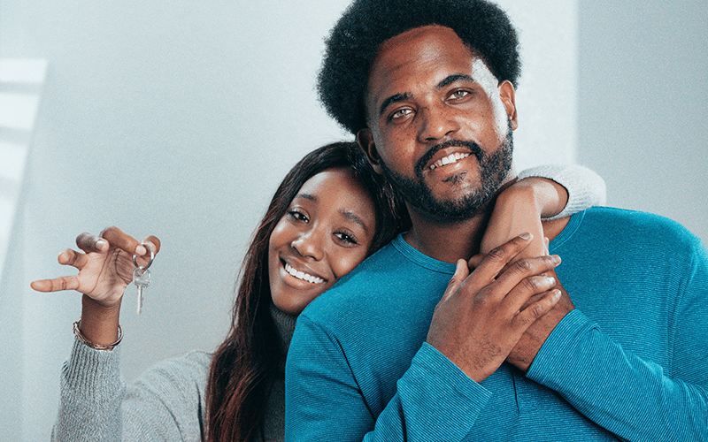 young black couple wearing blue holding keys to their new home