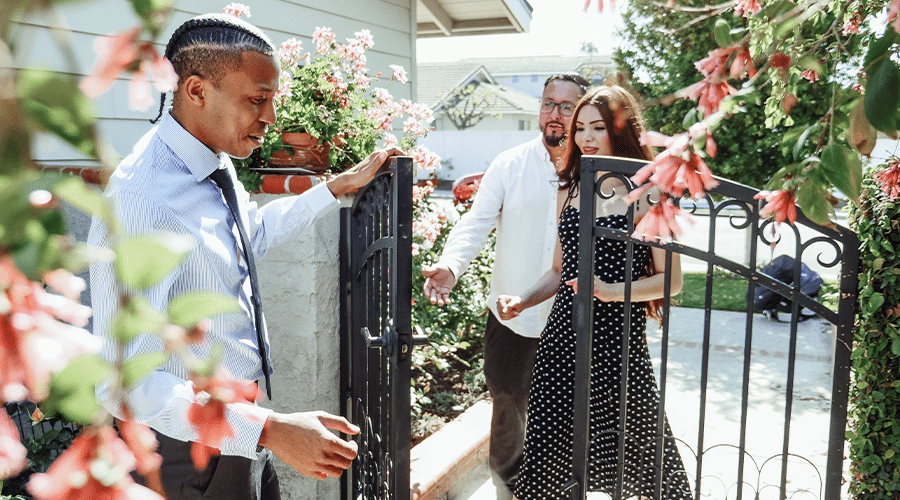african american male real estate agent opening gate to backyard for buyers with pink flowers