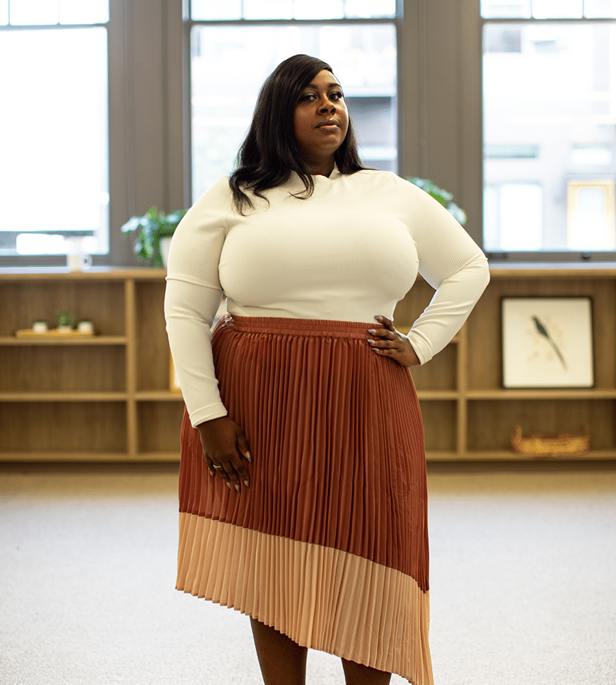 african american woman standing proudly with hand on hip in white top and pleated skirt