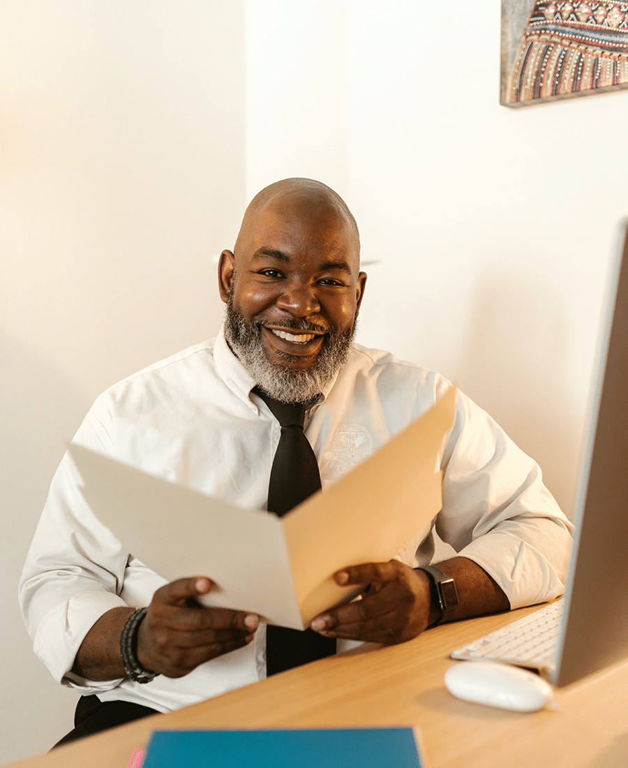 bald middle aged african american man with gray beard smiling at office desk holding folder