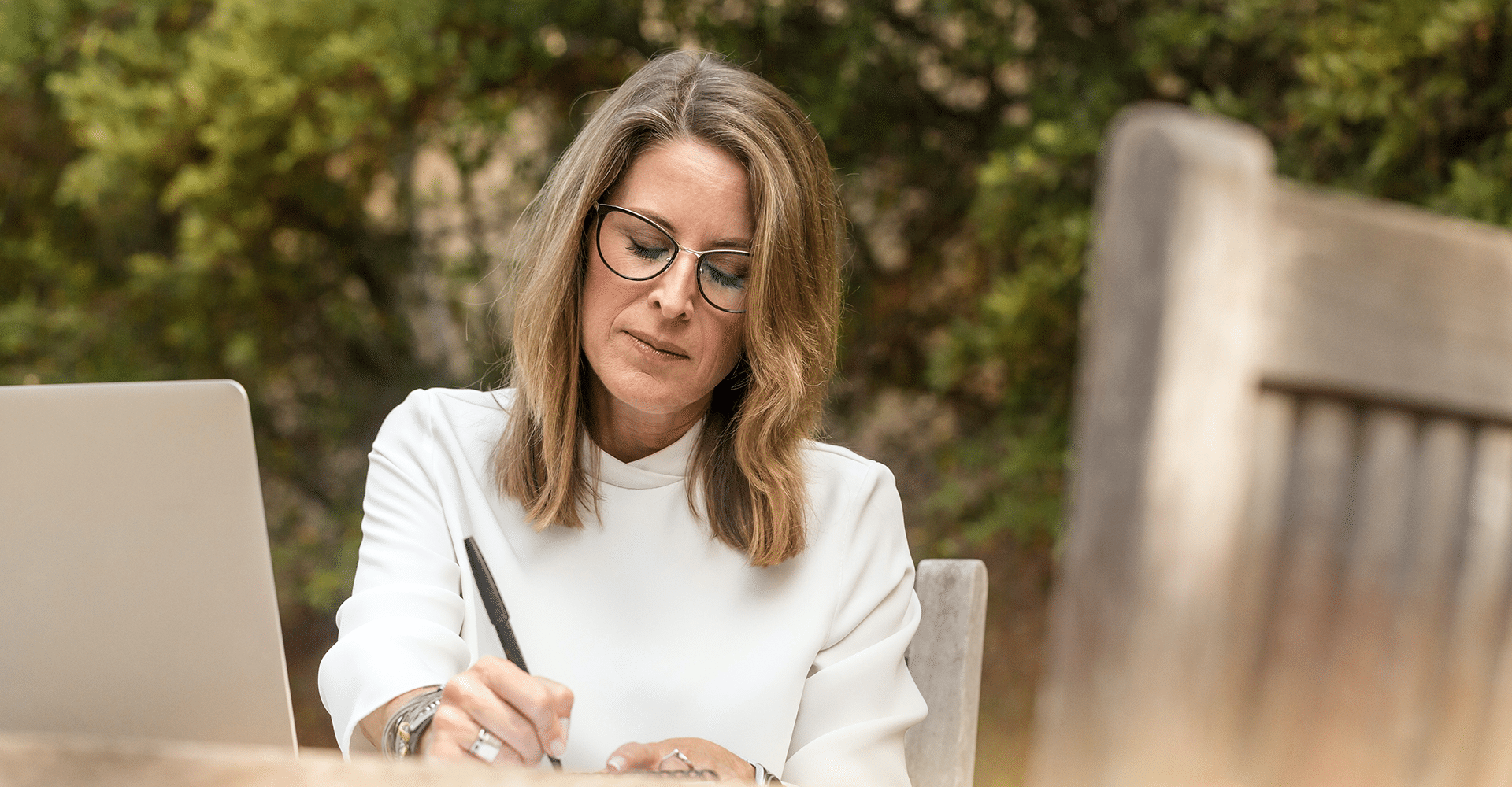 blonde caucasian woman in glasses writing note card to friend sitting outside