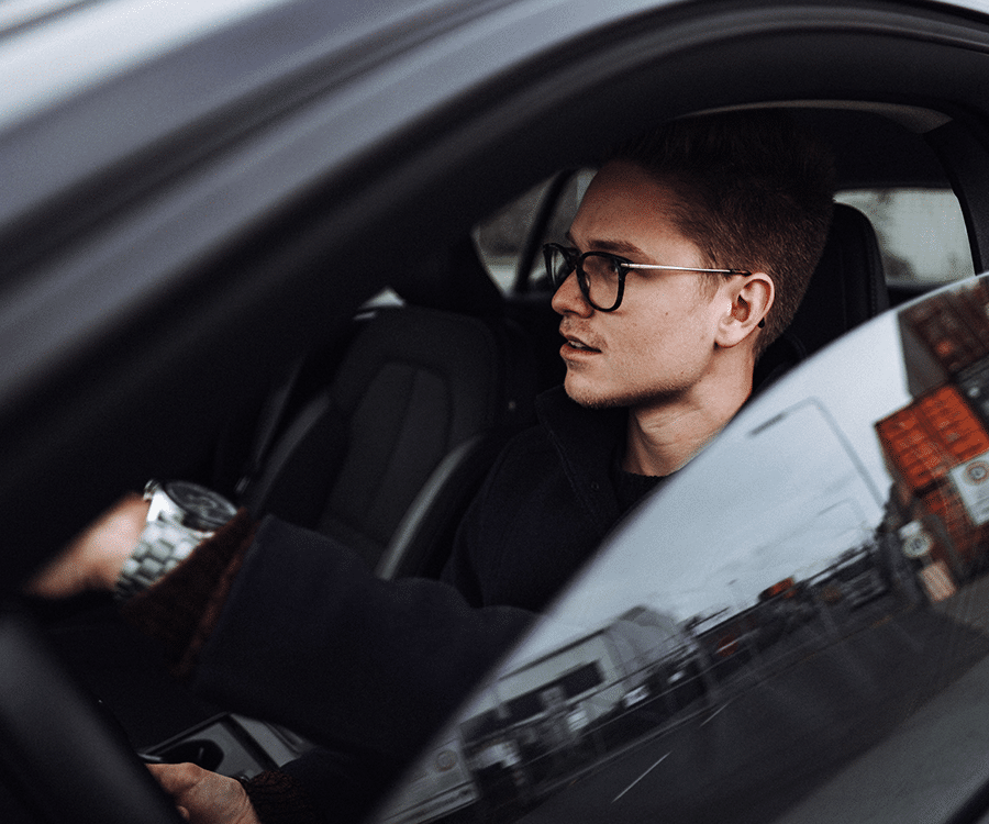 caucasian millennial man wearing black and glasses driving sedan car