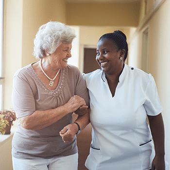 female nurse smiling with senior female patient holding her arm in hallway