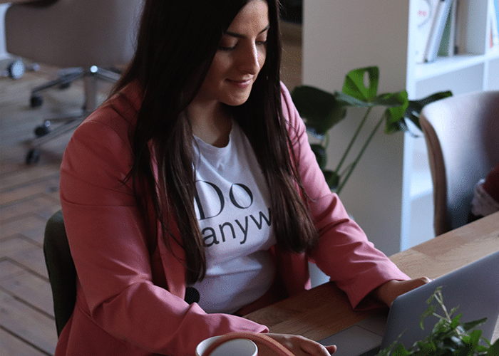 female real estate agent in graphic t-shirt and pink blazer on laptop in office with greenery