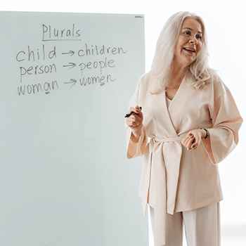 female teacher with white hair writing on dry erase board