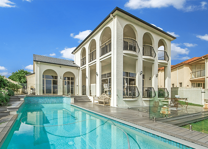 luxury two story home with balcony and bright blue swimming pool