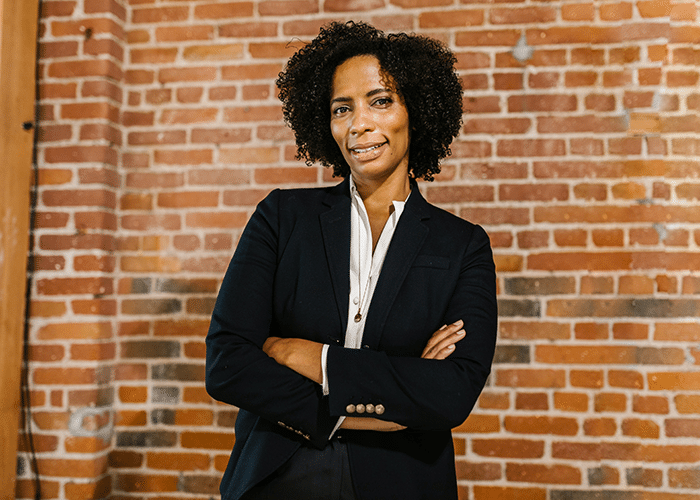 middle aged african american woman wearing suit with arms crossed against brick wall
