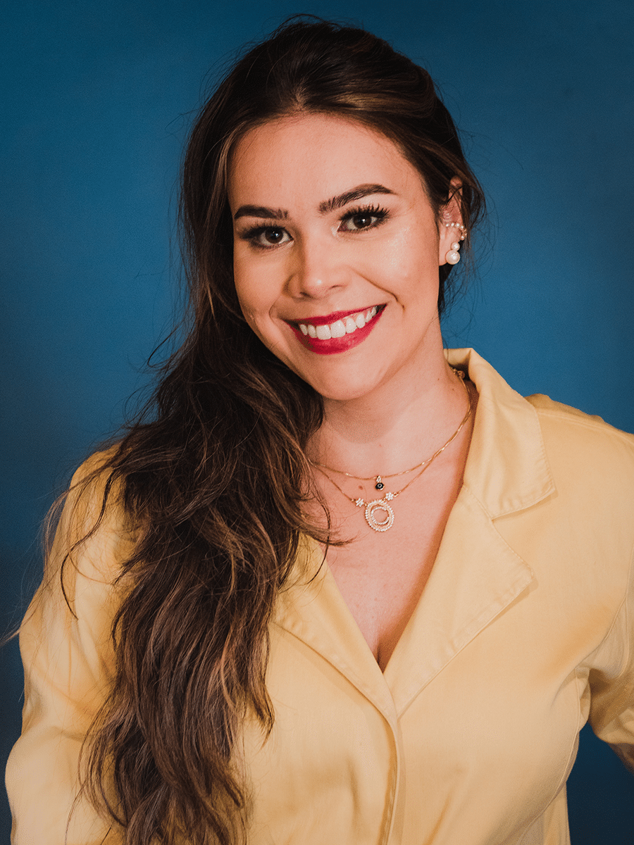 millennial female with long brown hair smiling wearing yellow blouse and red lipstick