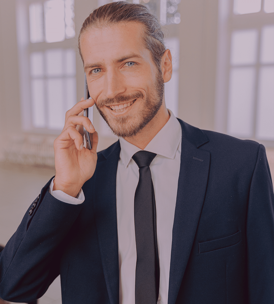 millennial man wearing suit and tie on cell phone smiling in white office