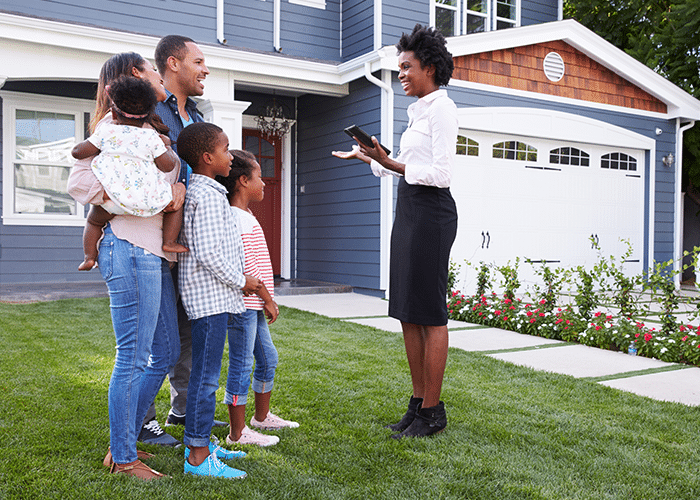 millennial female real estate agent showing family of five a home on the front lawn
