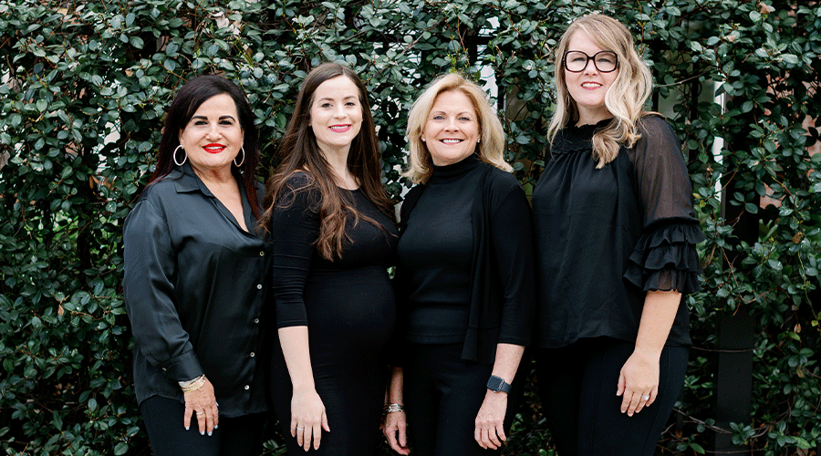 four-professionally-dressed-women-smiling-together-against-greener-on-wall-in-Florida