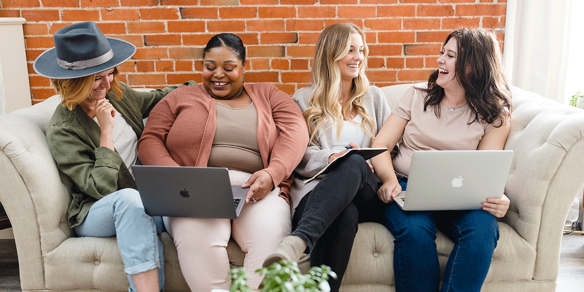 four-professional-women-sitting-on-a-couch-with-laptops-smiling