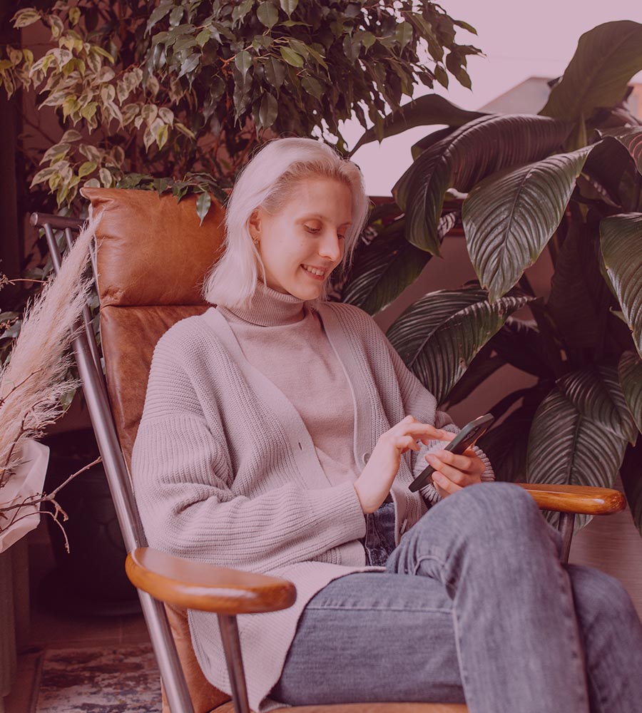 older white woman with white hair on smartphone sitting with plants around her